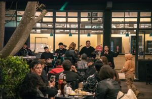 Clientes en las mesas de Bardo, en Tafí Viejo, mientras una banda toca en vivo detrás de la vidriera del local.