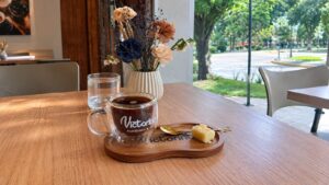 Taza de café y porción de pastel sobre tabla de madera con el logo de Victorino, pastelería y café en Tafí Viejo