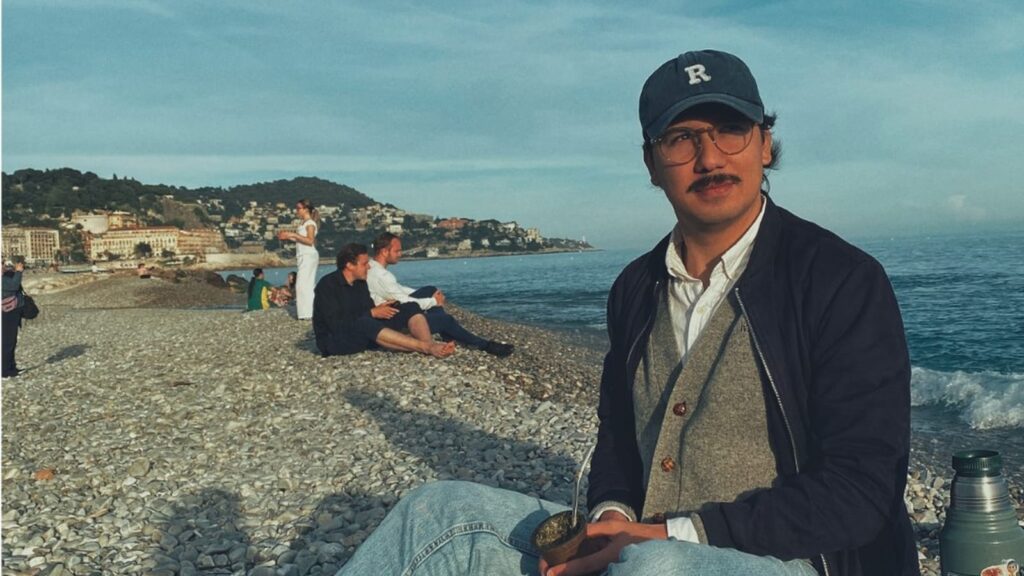 Facundo Benero, taficeño en Niza, toma mate sentado en una playa de piedras frente al mar